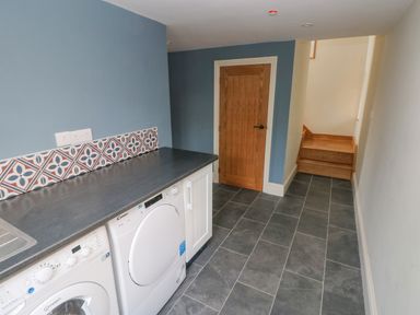 A laundry room with washing machine and dryer under a black countertop and a wooden door at the end of the room at Green Grove Barn in Peniel near Carmarthen