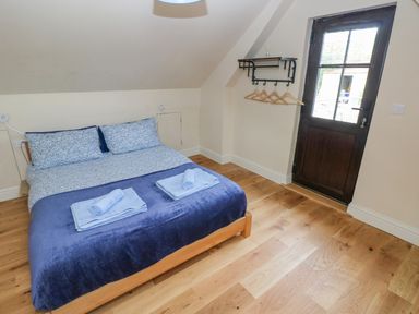 A bedroom with a double bed blue bedding towels on the bed wooden floor a door with window at Green Grove Barn Peniel near Carmarthen