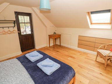 A bedroom with a bed with folded towels a wooden floor a small table a chair and a door at Green Grove Barn in Peniel near Carmarthen