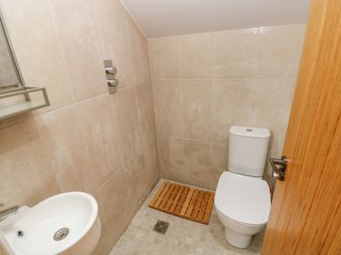 A small bathroom with a toilet sink and a wooden slatted mat on the tiled floor at Green Grove Barn in Peniel near Carmarthen