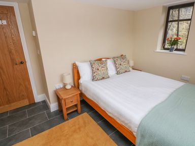 A bedroom with a wooden double bed with two patterned pillows two bedside tables with lamps a window with flowers on the sill and a wooden door at Green Grove Barn in Peniel near Carmarthen
