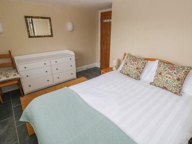 A bedroom with a bed with floral cushions a white dresser a wooden chair and a wooden door at Green Grove Barn in Peniel near Carmarthen