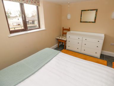 A bedroom with a bed near a window a white dresser a wooden chair with a cushion and a wall mirror at Green Grove Barn Peniel near Carmarthen