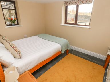 A bedroom with a wooden bed a side table with a lamp and two windows at Green Grove Barn Peniel near Carmarthen