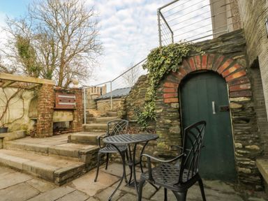 An outdoor patio area with metal table and chairs stone steps and a green door with a brick arch at Green Grove Barn in Peniel near Carmarthen