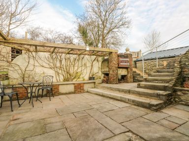 An outdoor patio with stone steps table and chairs brick oven and bare vines on a trellis at Green Grove Barn in Peniel near Carmarthen