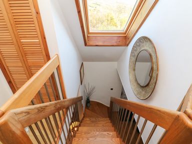A wooden staircase with metal railings under a skylight window and a round decorative mirror on the wall at Hillsview in Combe Martin