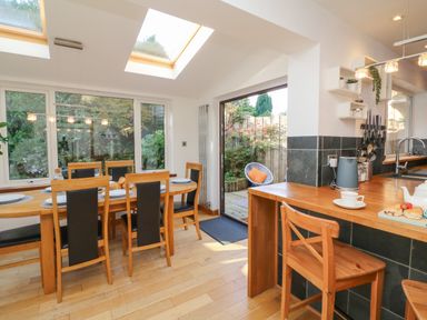 A dining area with a wooden table and chairs adjacent to a kitchen counter with a wooden chair at Hillsview in Combe Martin