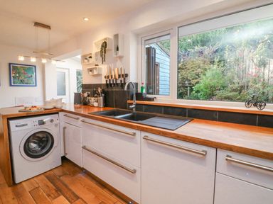 A kitchen with wooden countertops a washing machine a sink a window with a garden view and shelves with kitchen utensils at Hillsview in Combe Martin