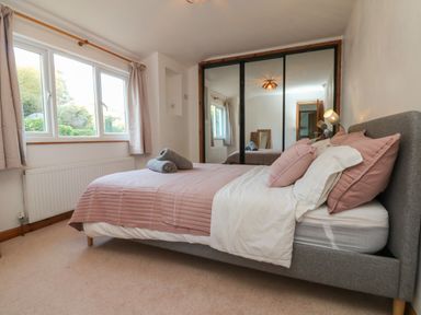 A bedroom with a bed covered with pink bedding and two gray towels on top a window with curtains and a mirrored wardrobe at Hillsview in Combe Martin