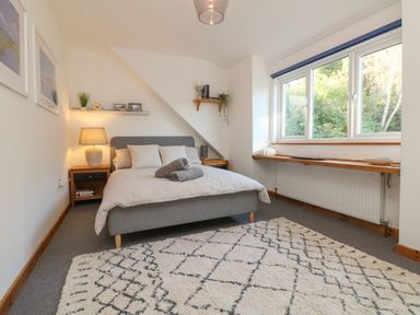 A bedroom with a bed and pillows a bedside table with a lamp and photographs a window with a wooden sill and a patterned rug on the floor at Hillsview in Combe Martin