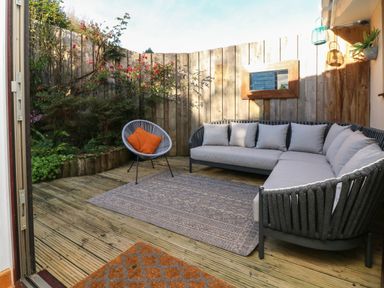 An outdoor patio with a gray sectional sofa a chair with orange pillows plants and a wooden fence at Hillsview in Combe Martin