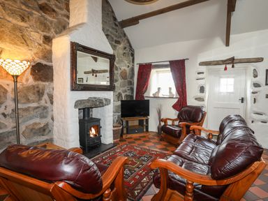A living room with leather chairs a fireplace a TV and red curtains at Tir Eironwy in Dinas near Nefyn