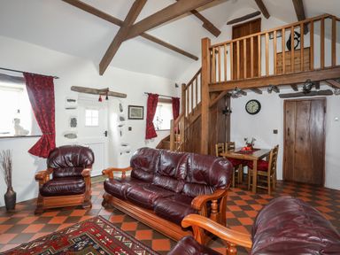 A living room with leather sofas a dining table wooden staircase and a loft at Tir Eironwy in Dinas near Nefyn