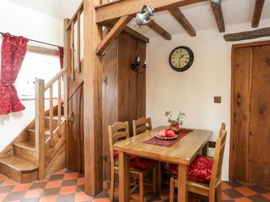 A dining area with wooden table and chairs by wooden stairs and a wall clock at Tir Eironwy in Dinas near Nefyn