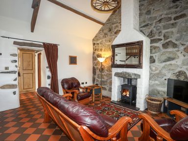 A living room with leather sofas a fireplace and a television at Tir Eironwy in Dinas near Nefyn