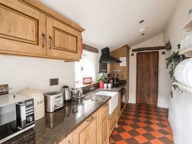 A narrow kitchen with wooden cabinets and a brown and orange tiled floor at Tir Eironwy in Dinas near Nefyn
