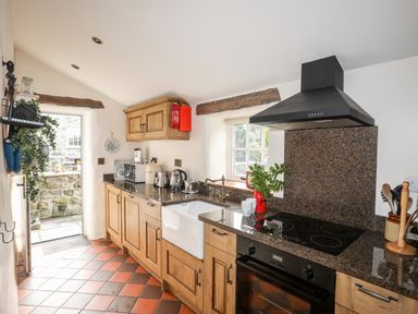 A kitchen with wooden cabinets a black stovetop a white sink and a door leading outside at Tir Eironwy Dinas near Nefyn