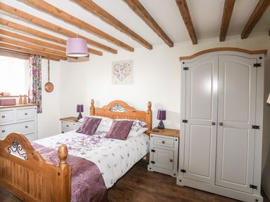 A bedroom with a wooden bed and purple bedding with matching lamps and white furniture at Tir Eironwy in Dinas near Nefyn