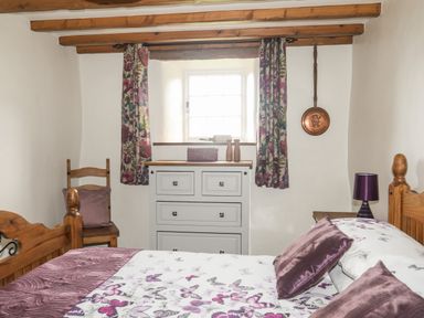 A bedroom with wooden bed and chair a white chest of drawers floral curtains and a window at Tir Eironwy in Dinas near Nefyn