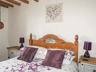 A bedroom with a wooden bed with butterfly bedding purple pillows and matching purple lamps on bedside tables at Tir Eironwy in Dinas near Nefyn