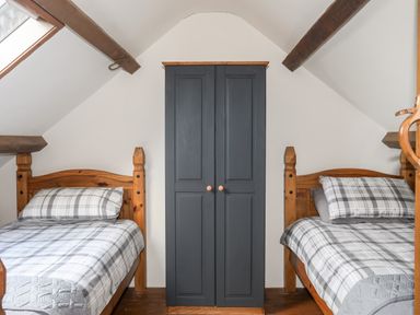 A bedroom with two single wooden beds with plaid bedding and a dark wardrobe in between at Tir Eironwy in Dinas near Nefyn