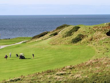 A golf course by the sea with golfers and a golf cart at Tir Eironwy in Dinas near Nefyn