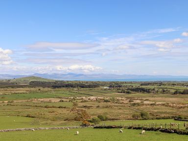 A rural landscape with green fields sheep and distant mountains at Tir Eironwy Dinas near Nefyn