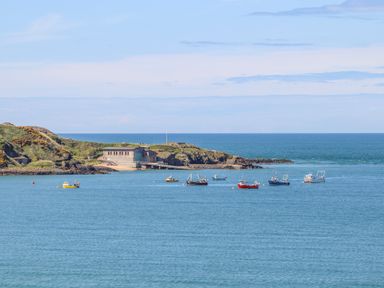 Boats moored in the sea near a rocky coastline with a building on the shore at Tir Eironwy in Dinas near Nefyn