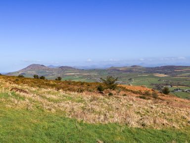 A landscape view with grassy fields and hills under a blue sky at Tir Eironwy in Dinas near Nefyn