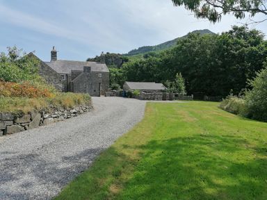 A stone house with gravel driveway next to a lawn and trees at Tir Eironwy in Dinas near Nefyn