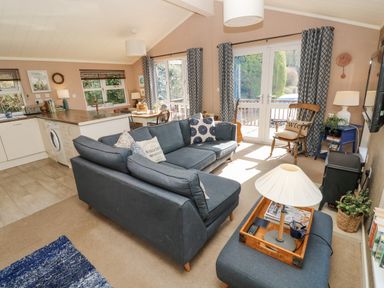A living room with a blue sofa set a wooden chair a lamp and a kitchen area in the background at 1 Hornbeam Lodge in Narberth