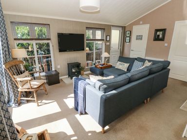 A living room with a blue sectional sofa a wooden chair a wall-mounted television and a small stove at 1 Hornbeam Lodge in Narberth