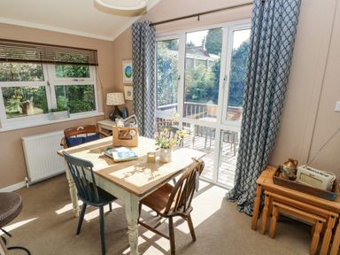 A dining area with a wooden table and mismatched chairs next to large windows and sliding glass doors at 1 Hornbeam Lodge in Narberth