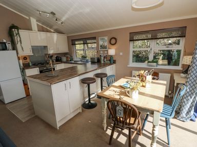 A kitchen with a wooden dining table and mixed chairs next to a countertop with stools at 1 Hornbeam Lodge in Narberth