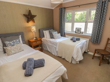 A bedroom with two single beds a wooden nightstand with a lamp a wicker star on the wall and a wooden chair at 1 Hornbeam Lodge in Narberth