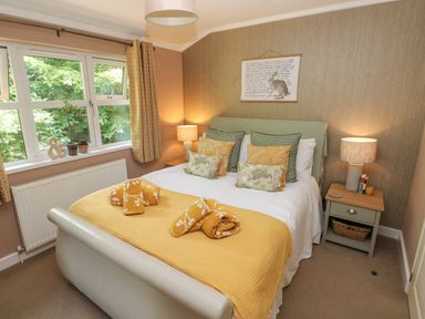 A bedroom with a bed with yellow and patterned cushions bedside tables with lamps and a window with curtains at 1 Hornbeam Lodge in Narberth
