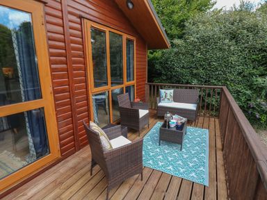 A wooden deck with three chairs a small table with cups and a teapot and a blue patterned rug at 1 Hornbeam Lodge in Narberth