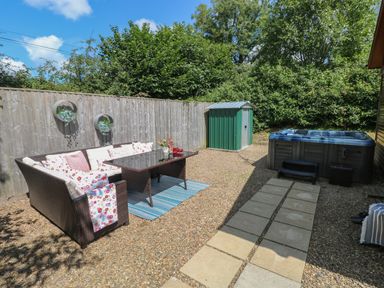 An outdoor seating area with a wicker sofa and table near a shed and a hot tub at 1 Hornbeam Lodge in Narberth