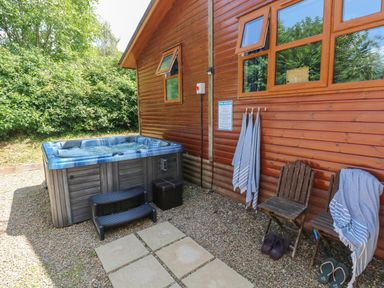 An outdoor area with a hot tub, two wooden chairs, towels hanging on hooks, and two pairs of sandals at 1 Hornbeam Lodge in Narberth