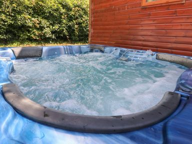 An outdoor hot tub with bubbling water next to a wooden wall and green bushes at 1 Hornbeam Lodge in Narberth