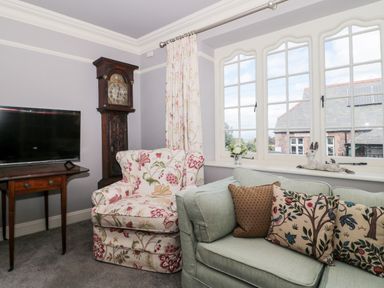 A living room with a floral armchair wooden grandfather clock television on table and light green sofa with patterned cushions by a window at The Pound in Porlock