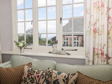 A window with floral curtains and a figurine on the windowsill above a sofa with patterned cushions at The Pound in Porlock