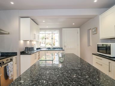 A kitchen with a black granite countertop island, white cabinets, a stainless steel oven, a microwave, and a window above the sink at The Pound in Porlock