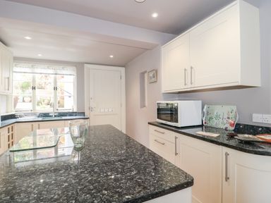 A kitchen with granite countertops white cabinets a microwave and a glass on the counter at The Pound in Porlock