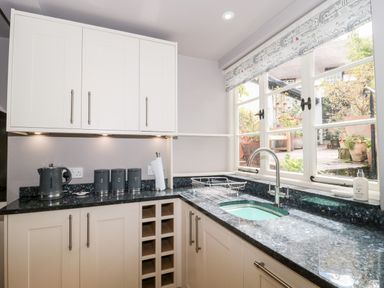 A kitchen corner with white cabinets black countertop a sink a kettle canisters and a window showing an outdoor patio at The Pound in Porlock