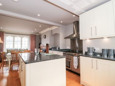 A kitchen with white cabinets a black countertop a stainless steel stove and hood and a dining table with chairs at The Pound in Porlock