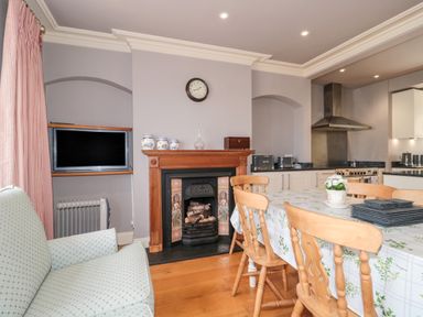 A kitchen and dining area with wooden chairs around a table next to a fireplace and a flat screen tv on the wall at The Pound in Porlock