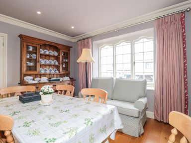 A dining room with a wooden table and chairs a sofa a wooden cabinet with dishes a floor lamp and windows with curtains at The Pound in Porlock