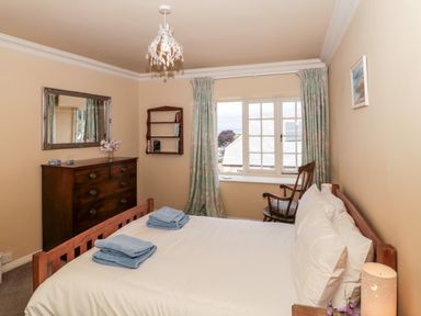 A bedroom with a wooden bed a chest of drawers a chair a window with curtains and a wall mirror at The Pound in Porlock
